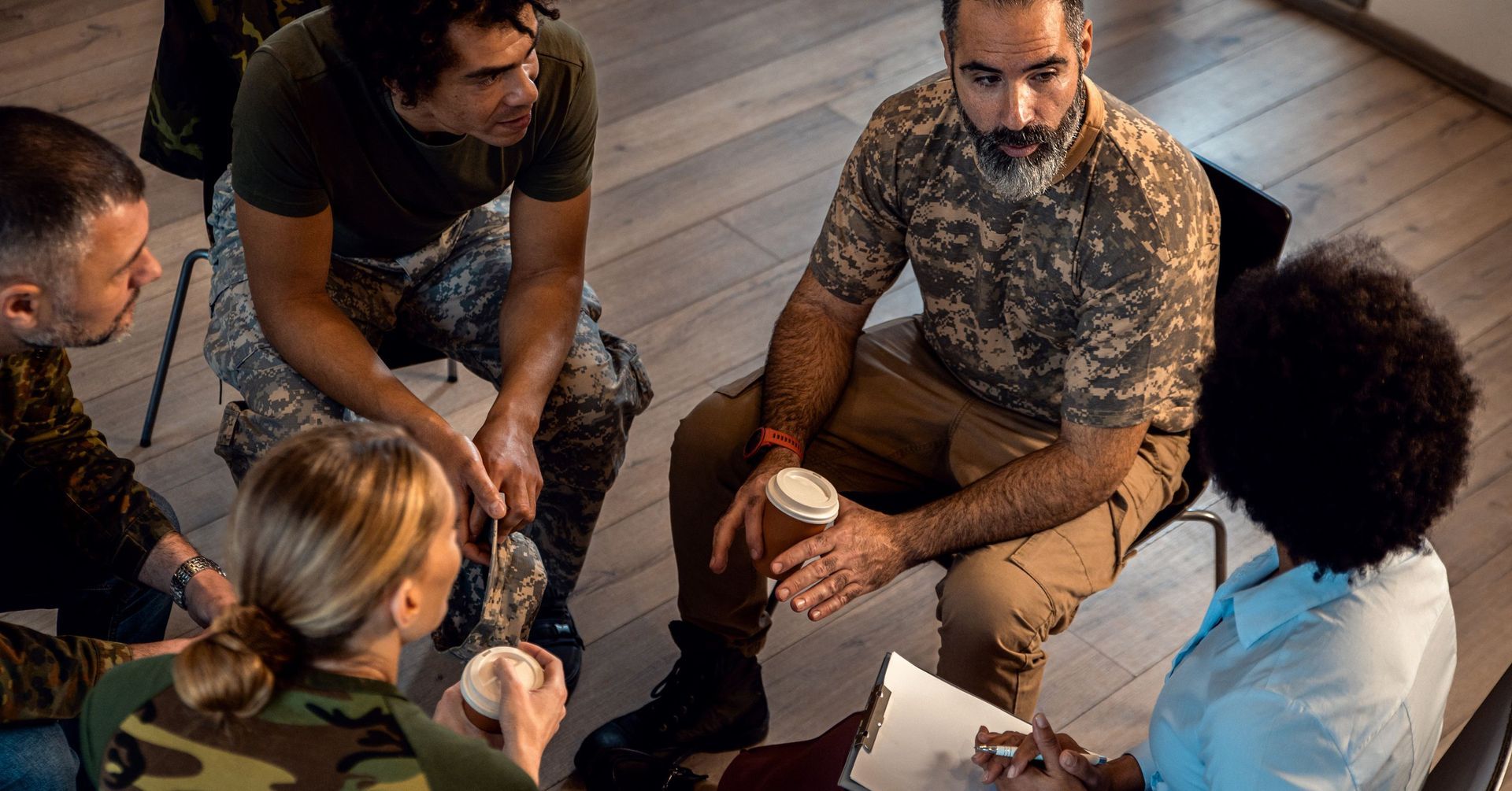 A diverse group of veterans in camouflage attire sitting in a circle during a home accessibility aud
