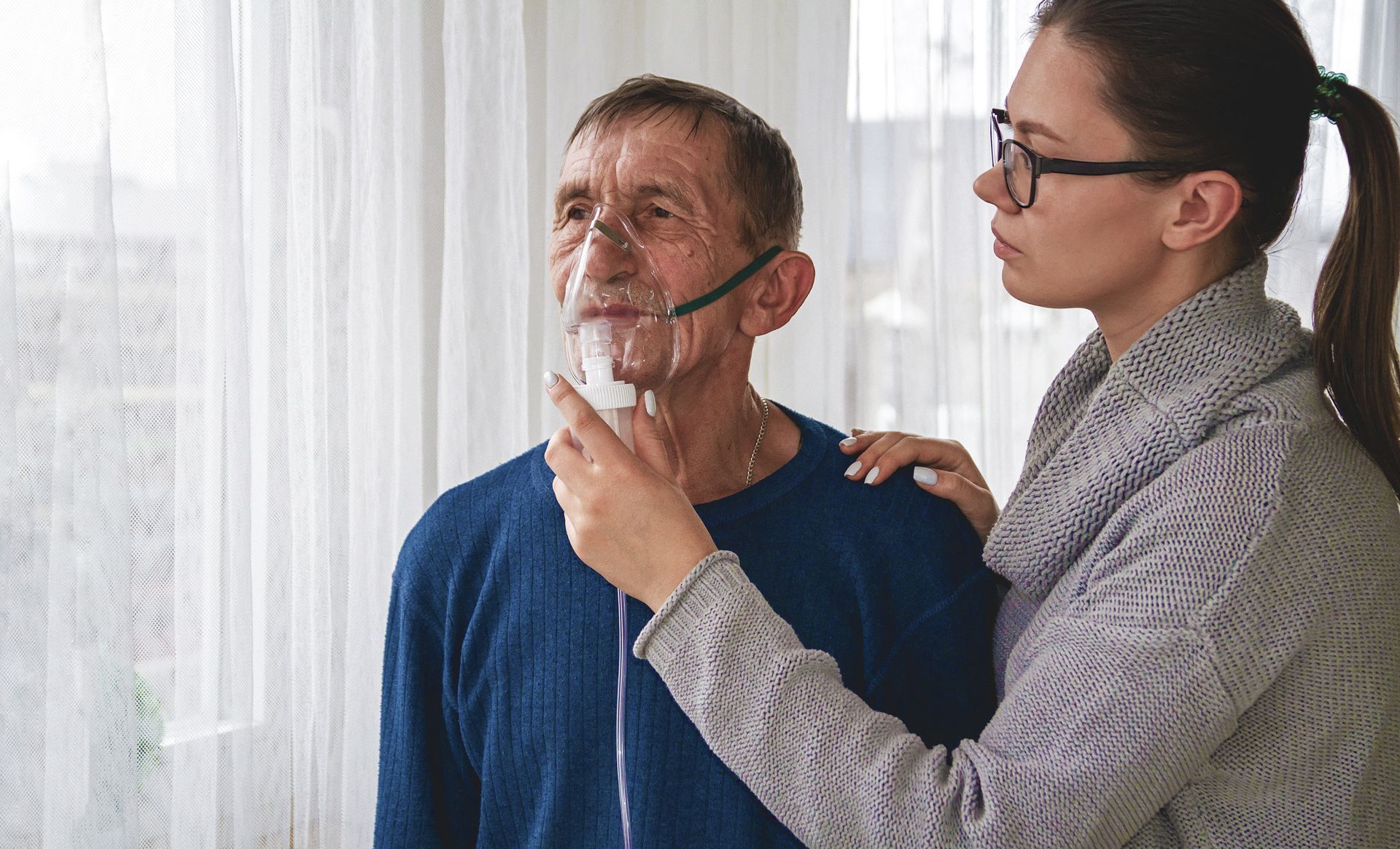 A woman is helping an elderly man wear an oxygen mask.