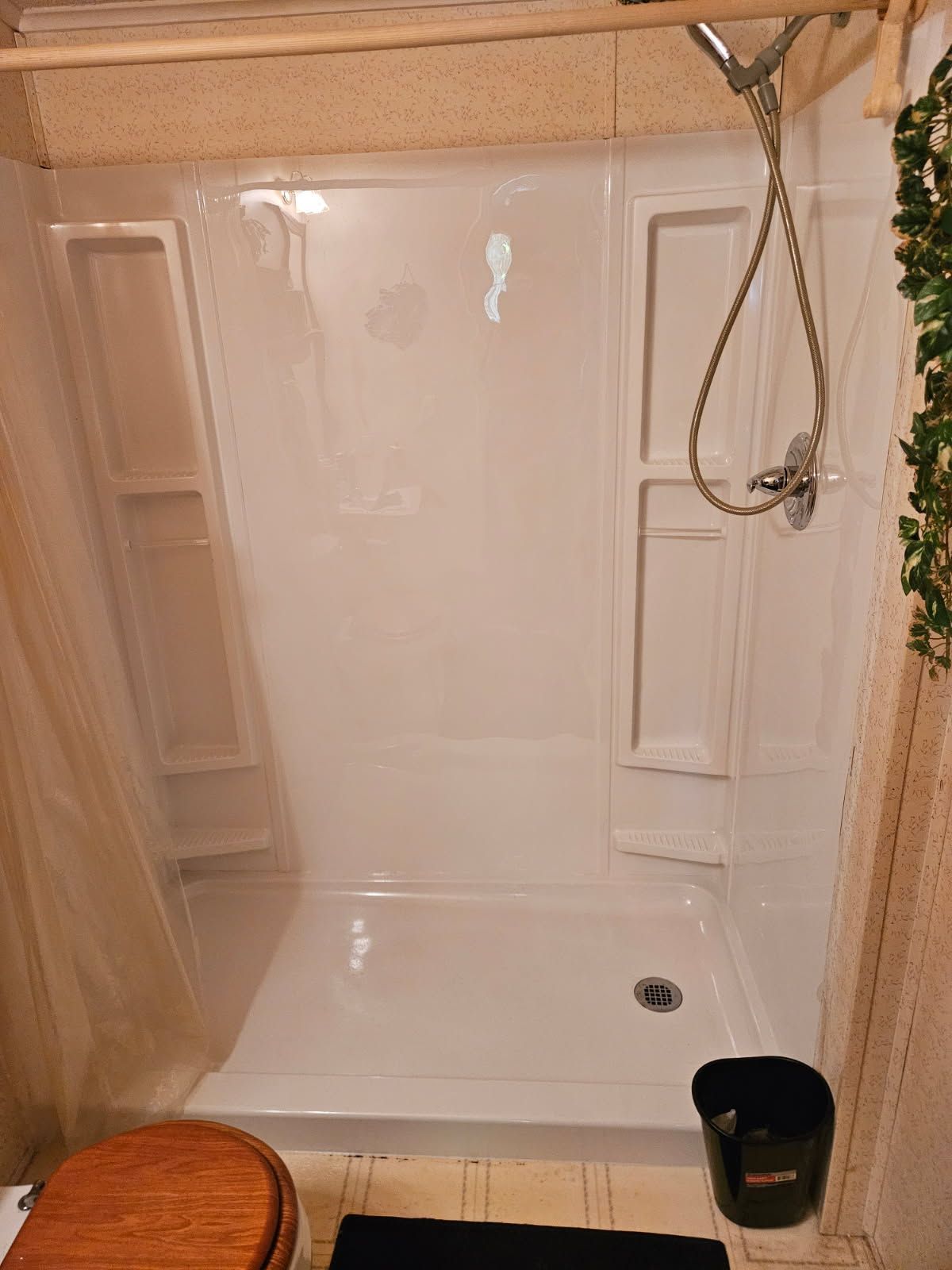 A white fiberglass shower stall with built-in shelving, a flexible handheld shower head, and a drain on the floor.