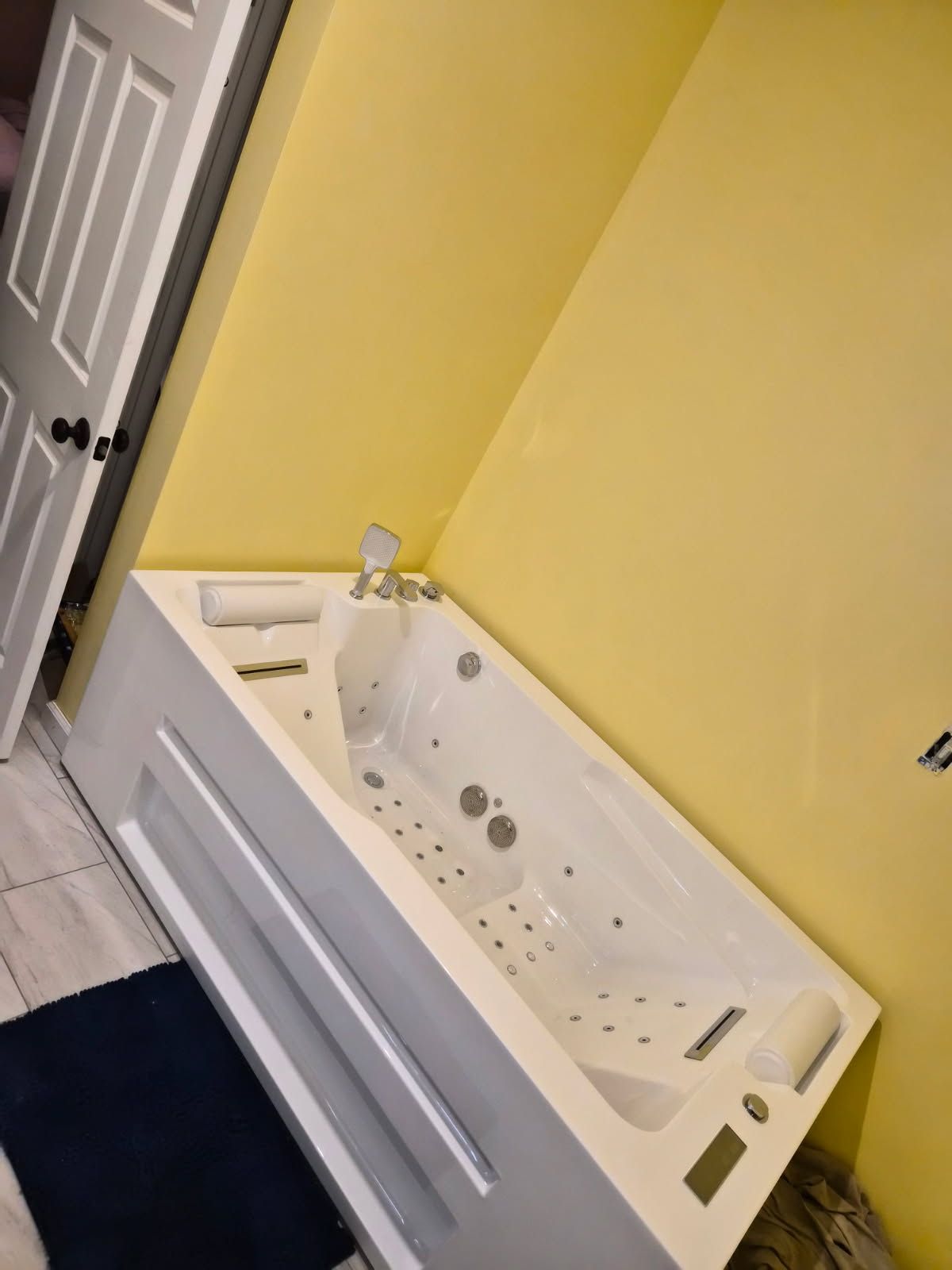 A white jetted bathtub with headrests and fixtures, set against yellow walls in a bathroom with light-colored tile floors.