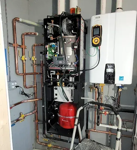 HVAC boiler and tankless water heater setup with copper pipes, a red expansion tank, and a diagnostic tool attached.