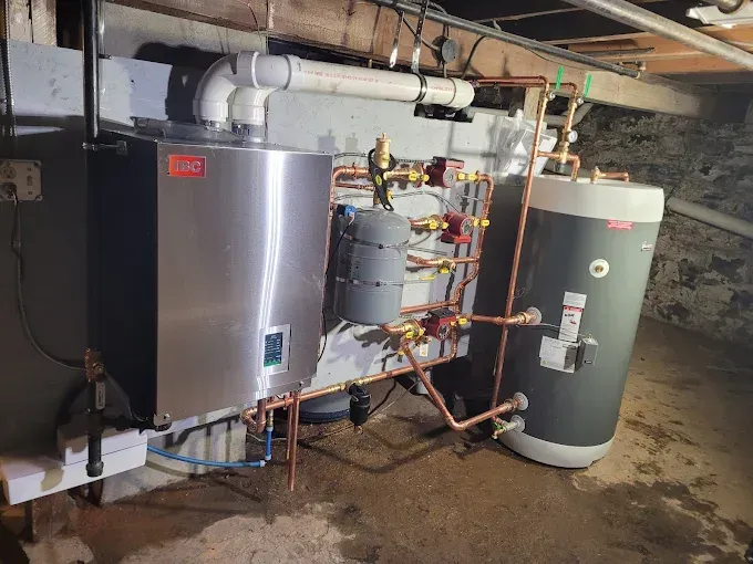 A high-efficiency wall-mounted boiler and a cylindrical water storage tank installed in a residential basement.