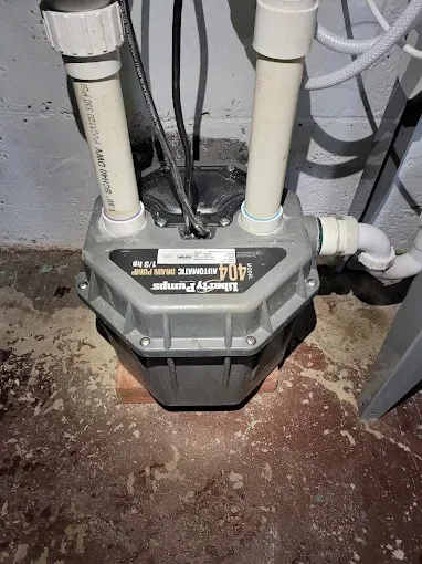 A gray Liberty Pumps 404 automatic drain pump unit installed on a concrete floor with PVC piping connected to the top.