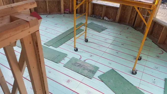 Construction site with green radiant floor insulation panels and red heating tubes installed on the floor.