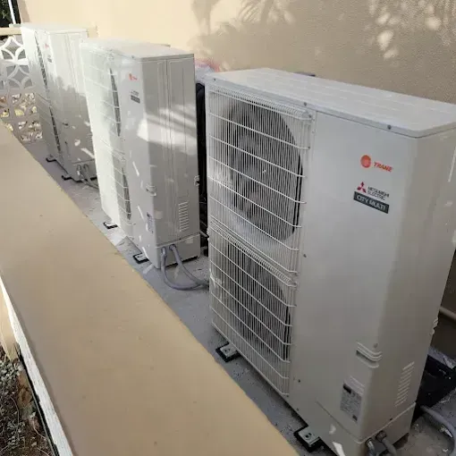 A row of three white outdoor air conditioning units lined up against an exterior wall.