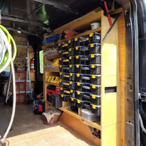 A wooden shelving unit inside a cargo van, featuring rows of stacked black plastic organizers with yellow latches.