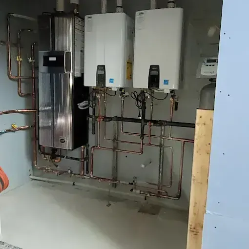 A utility room containing a boiler and two wall-mounted tankless water heaters connected by copper plumbing.