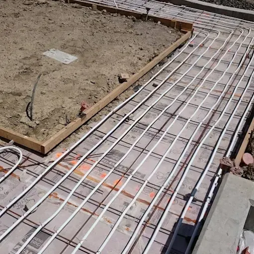 Radiant floor heating tubing installed in a grid pattern on insulation over a construction site.
