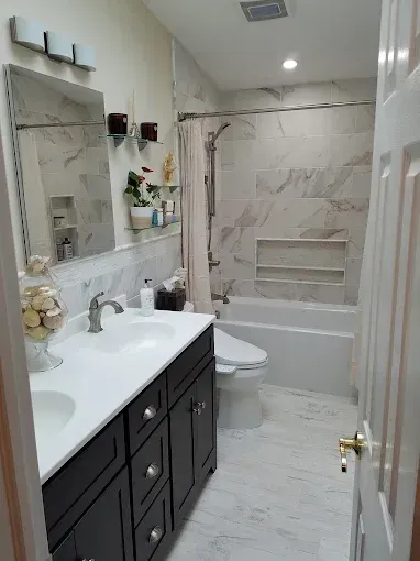 A modern bathroom with a dark wood vanity, white countertop, silver mirror, and a tub-shower with marble-style tiles.