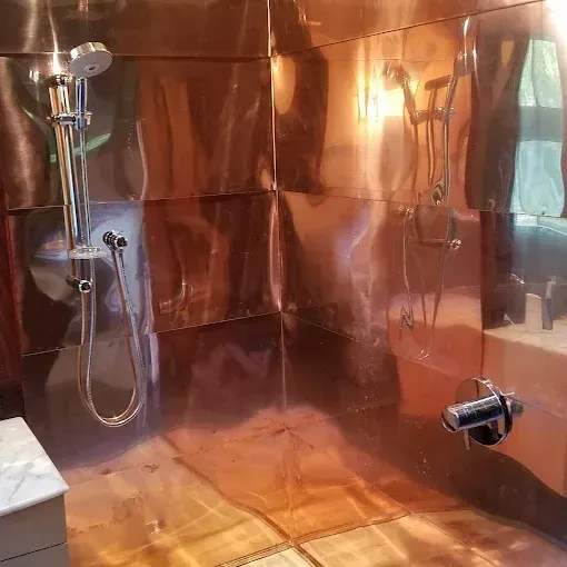 Modern walk-in shower with polished copper wall panels, a chrome handheld showerhead, and a matching wall-mounted faucet.