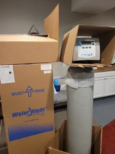 Water-Right water treatment equipment, including a tall filter tank and control valve in cardboard packaging indoors.