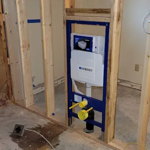 Wall-mounted toilet frame and white Geberit flush tank installed between wooden wall studs during construction.