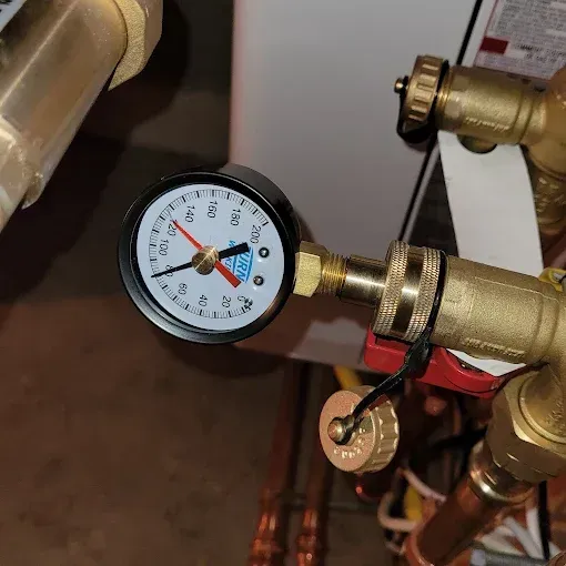 A close-up of a circular analog pressure gauge with a red needle pointing to approximately 30 psi, attached to brass piping.