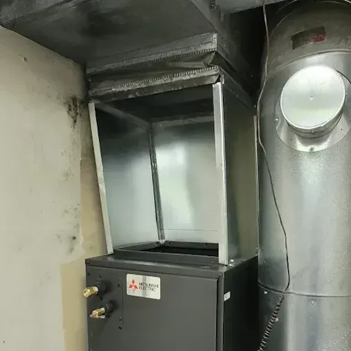 A Mitsubishi Electric indoor HVAC air handler unit connected to a metal duct system in a utility space.