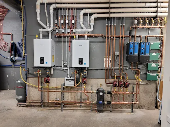 Wall-mounted boilers, white piping, and copper plumbing manifolds installed in a utility room.