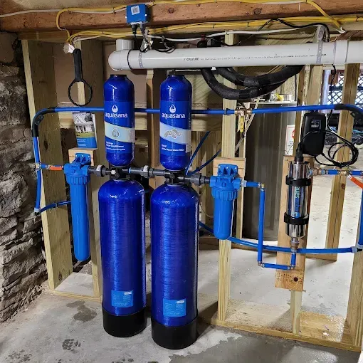 A home water filtration system with two blue tanks, two blue cartridge housings, and a UV light mounted on a wooden frame.