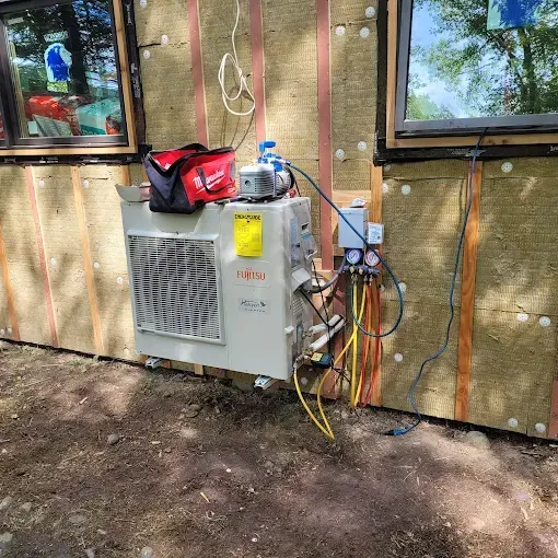 A Fujitsu mini-split condenser unit mounted on an exterior wall, connected to a vacuum pump and manifold gauges.
