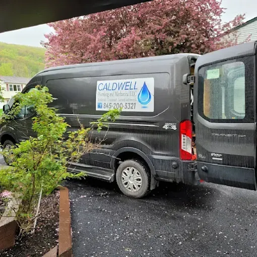 A dark gray Caldwell Plumbing and Water van parked on a driveway with its rear passenger-side door open.
