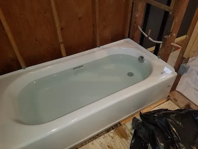 A new white bathtub filled with water installed in a room under construction with exposed wooden wall studs.