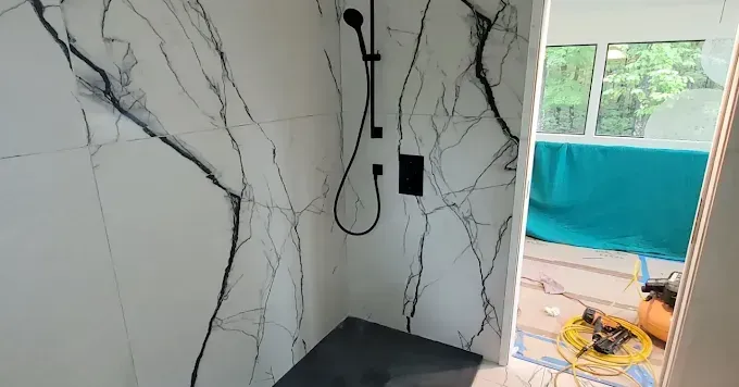 A shower featuring large-format white marble tiles with black veining, a matte black rainfall showerhead, and a dark base.