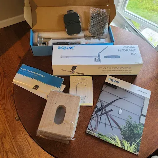 An Aquor house hydrant kit box, manuals, and installation components spread out on a wooden table.