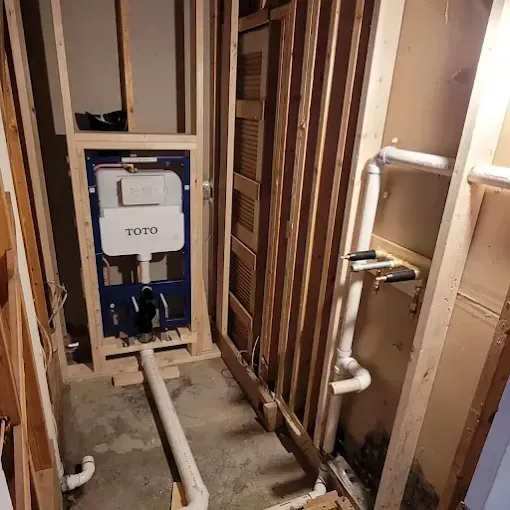A bathroom renovation showing a wall-mounted TOTO toilet tank installed in wooden framing with exposed PVC plumbing pipes.