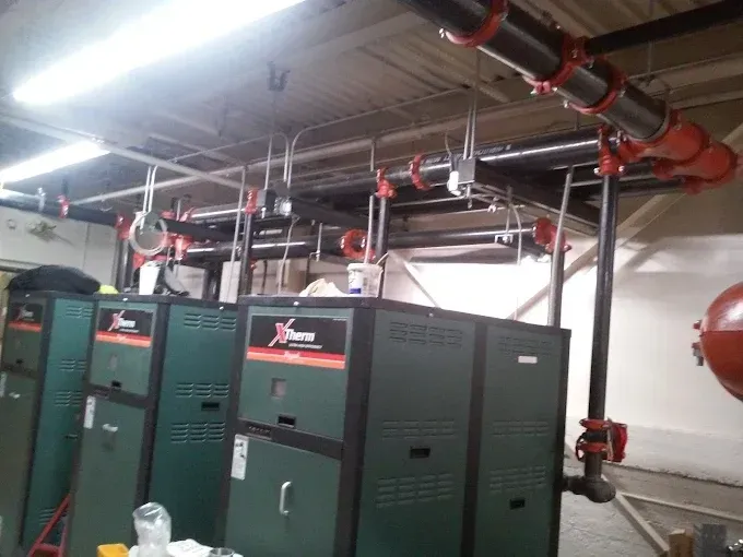 Industrial boiler room with dark green Vance brand units and red-coupled overhead pipes suspended from the ceiling.
