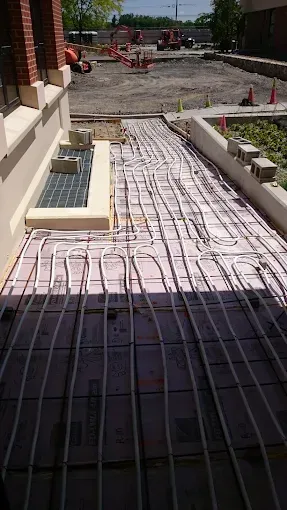 White PEX tubing laid out in a grid pattern over insulation boards at an outdoor construction site.
