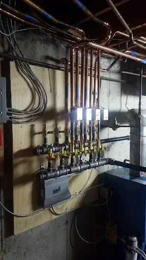 A plumbing manifold system with copper pipes, yellow-handled valves, and electrical wiring mounted on a plywood board.