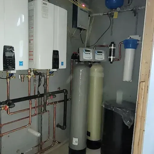 Utility room featuring two tankless water heaters, a water filtration system, and two large tanks with digital controllers.