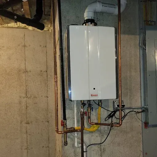 A white wall-mounted tankless water heater with copper piping and a yellow gas line installed in a basement.