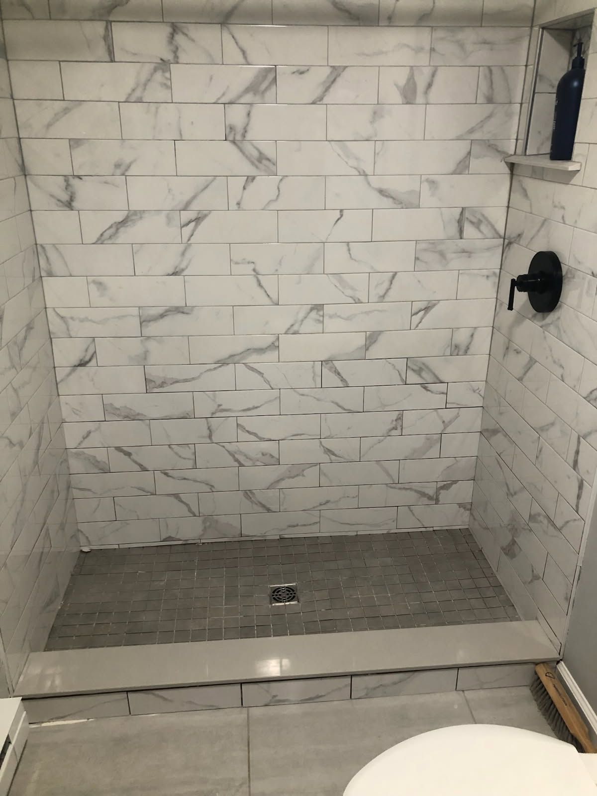 A tiled walk-in shower with white marbled subway tiles on the walls and grey textured tiles on the floor.