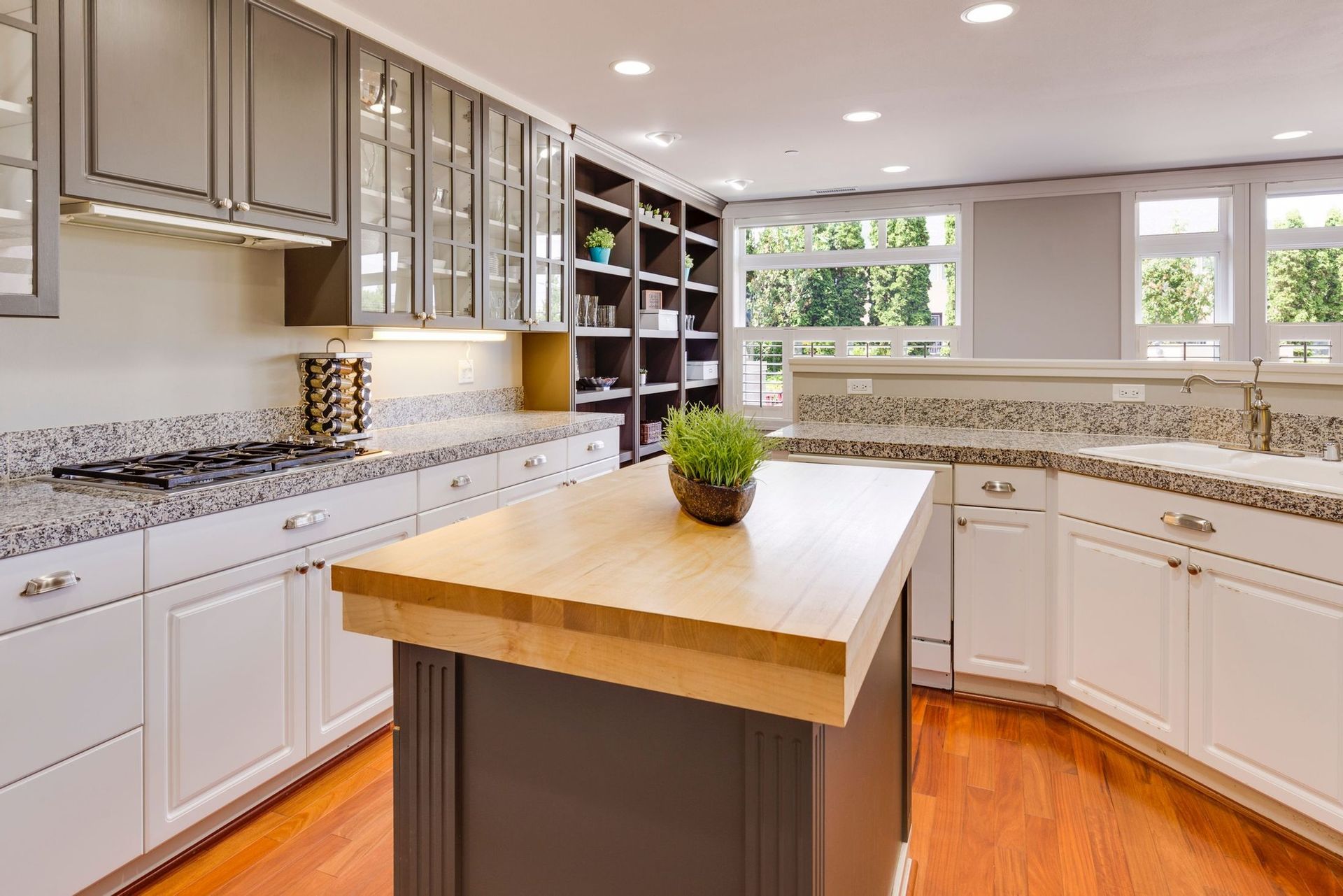 a kitchen with white cabinets , granite counter tops , and a wooden island .