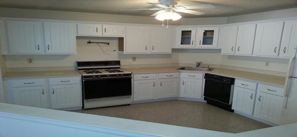 A kitchen with white cabinets , black appliances and a ceiling fan.
