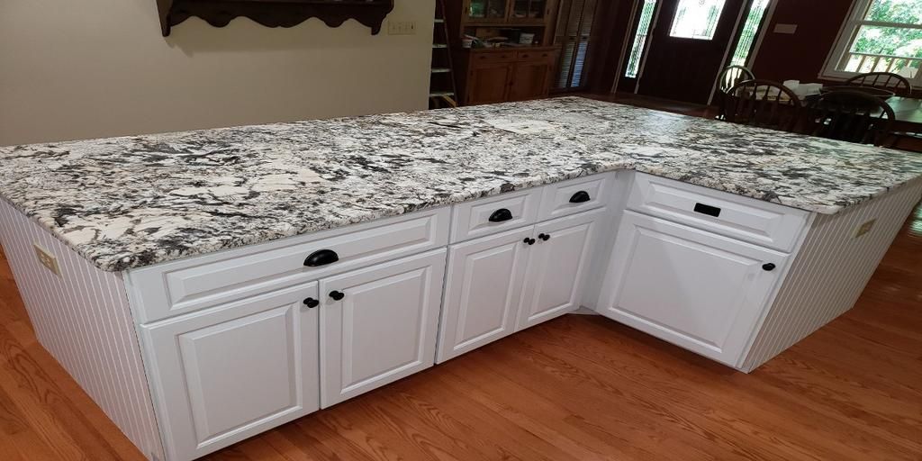 A kitchen island with granite counter tops and white cabinets.