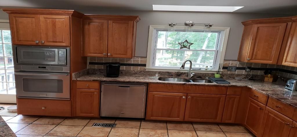 A kitchen with wooden cabinets , granite counter tops , stainless steel appliances and a window.