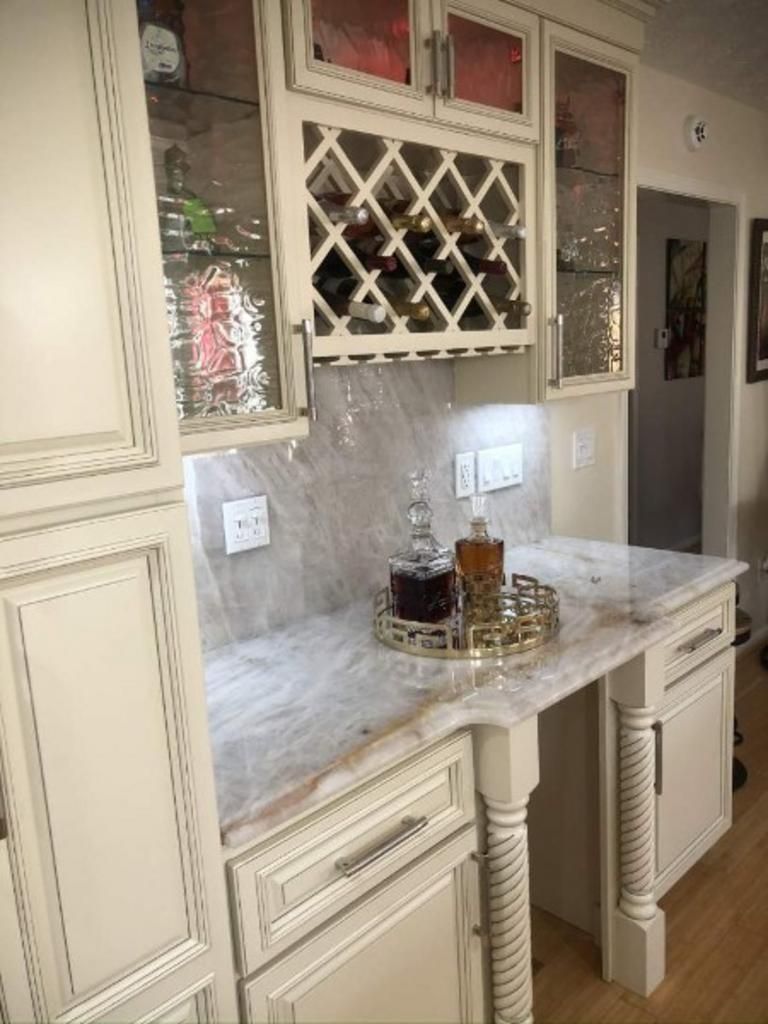 A kitchen with white cabinets , marble counter tops , and a wine rack.