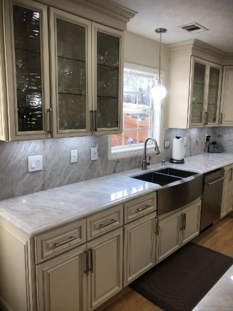 A kitchen with white cabinets , white counter tops , a sink and a window.