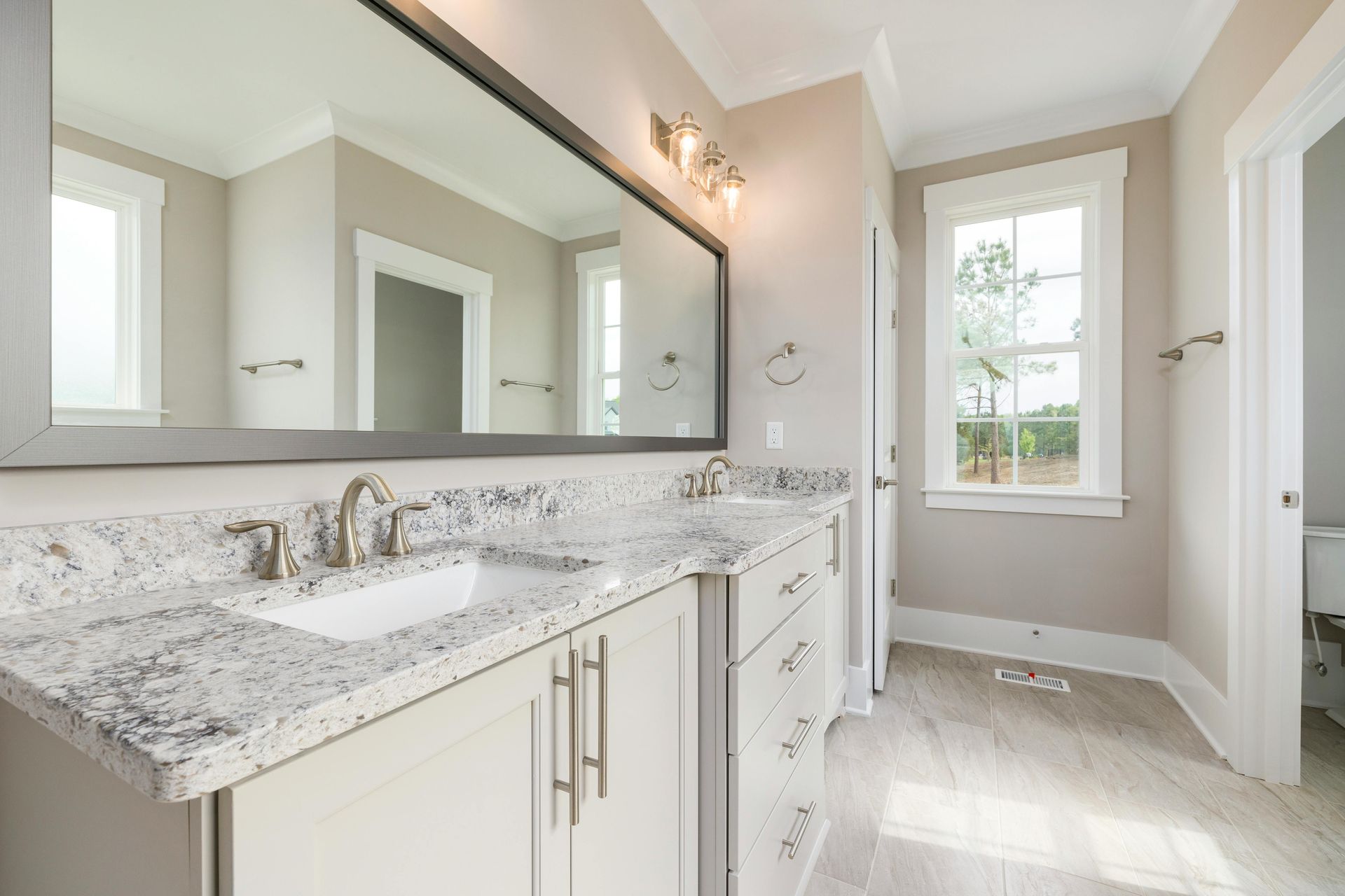 Bathroom with a gray vanity, granite countertop, large mirror, and a window with sunlight.
