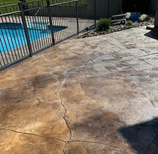 A concrete patio with a fence and a pool in the background.