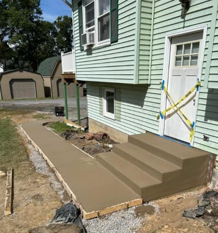 A green house with concrete steps being built in front of it.