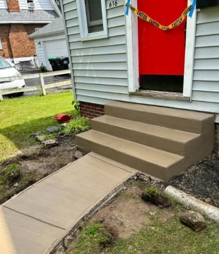 A concrete walkway with stairs leading up to the front door of a house.