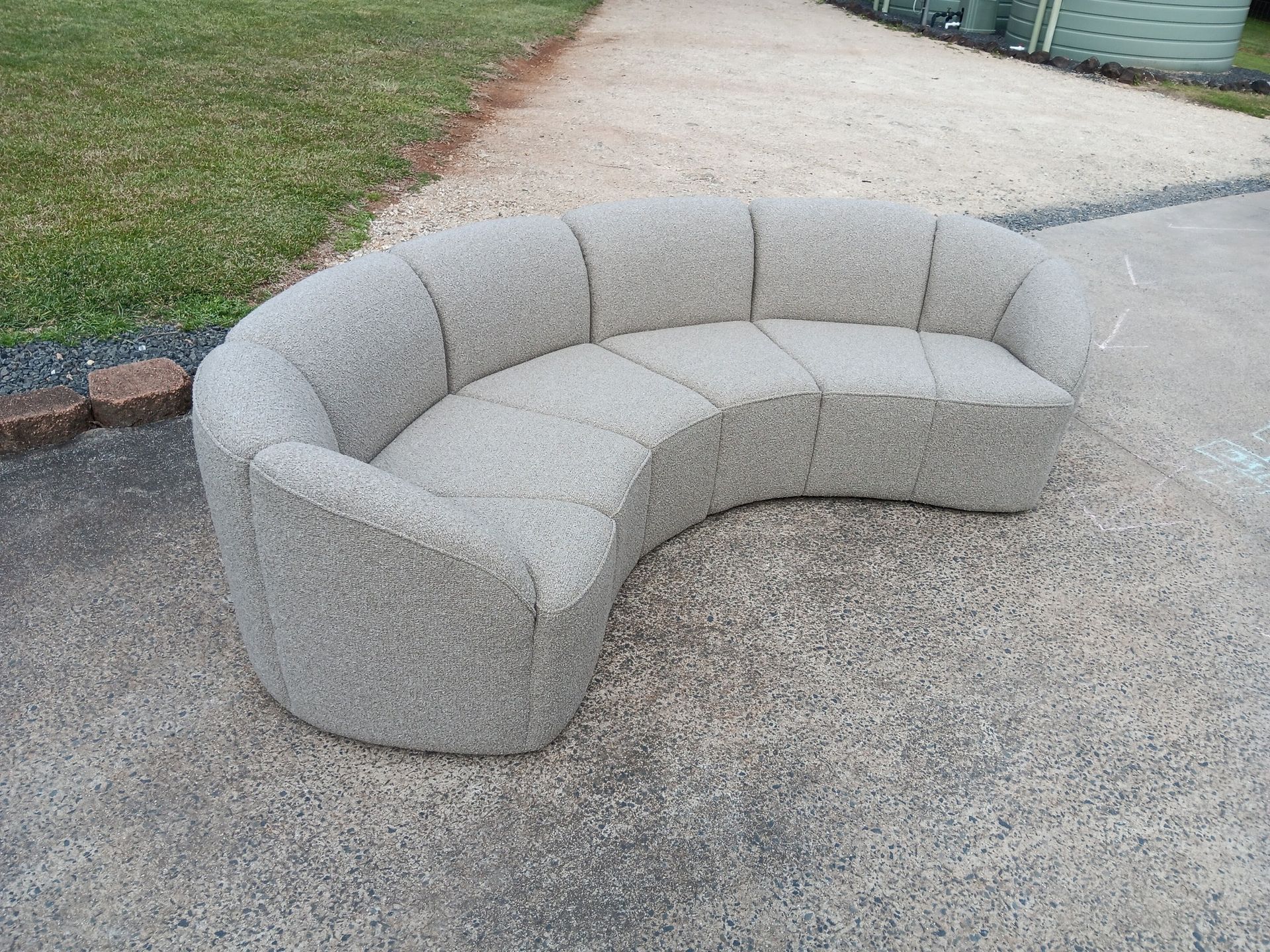 A Curved, Gray Textured Sofa on a Gravel Surface, Outdoors — Cupitt's Quality Upholstery in Rous, NSW