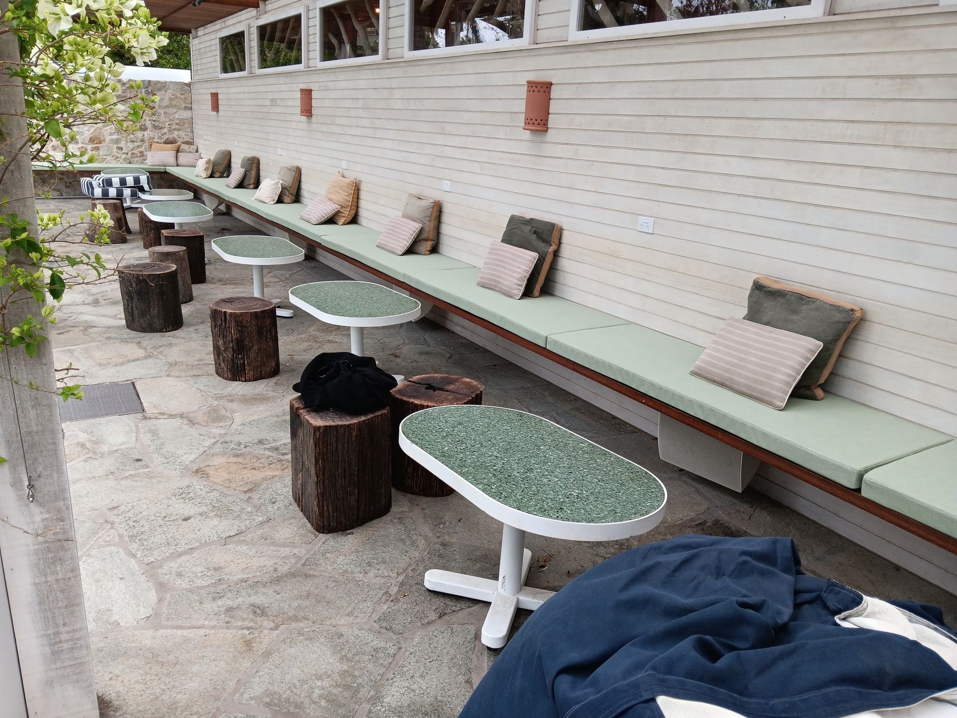 Outdoor seating area with benches, small tables, tree stump stools, and cushions.