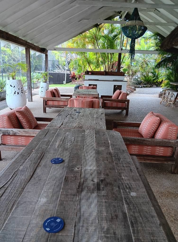 Outdoor lounge area with wooden furniture, red cushions, and a view of lush greenery.