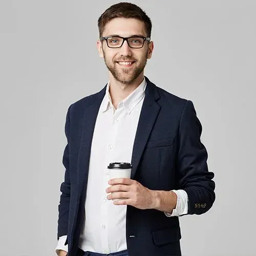 Man in a blazer and glasses smiles, holding coffee cup against a gray background.