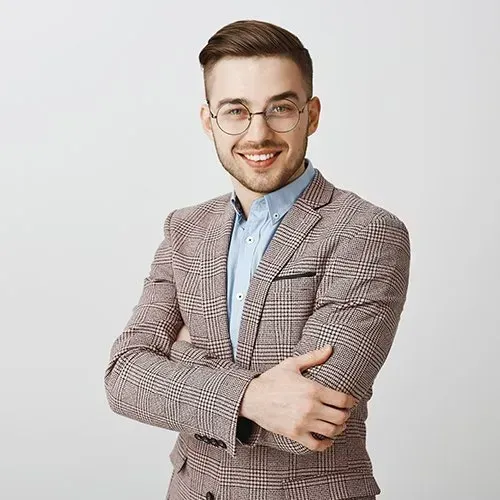 Young man with glasses smiles, arms crossed, wearing a plaid suit and blue shirt.