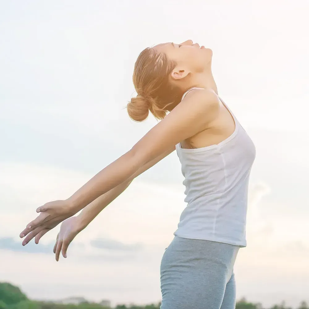 Woman in athletic wear with arms outstretched, face tilted upward, outdoors.