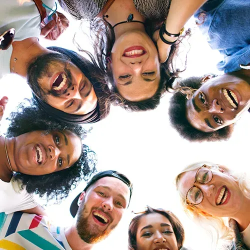 Group of diverse people smiling in a circle, looking down at the viewer.