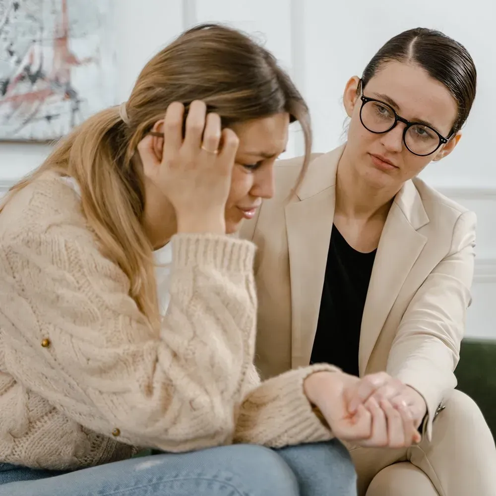 Woman in distress, comforted by another woman, indoors.